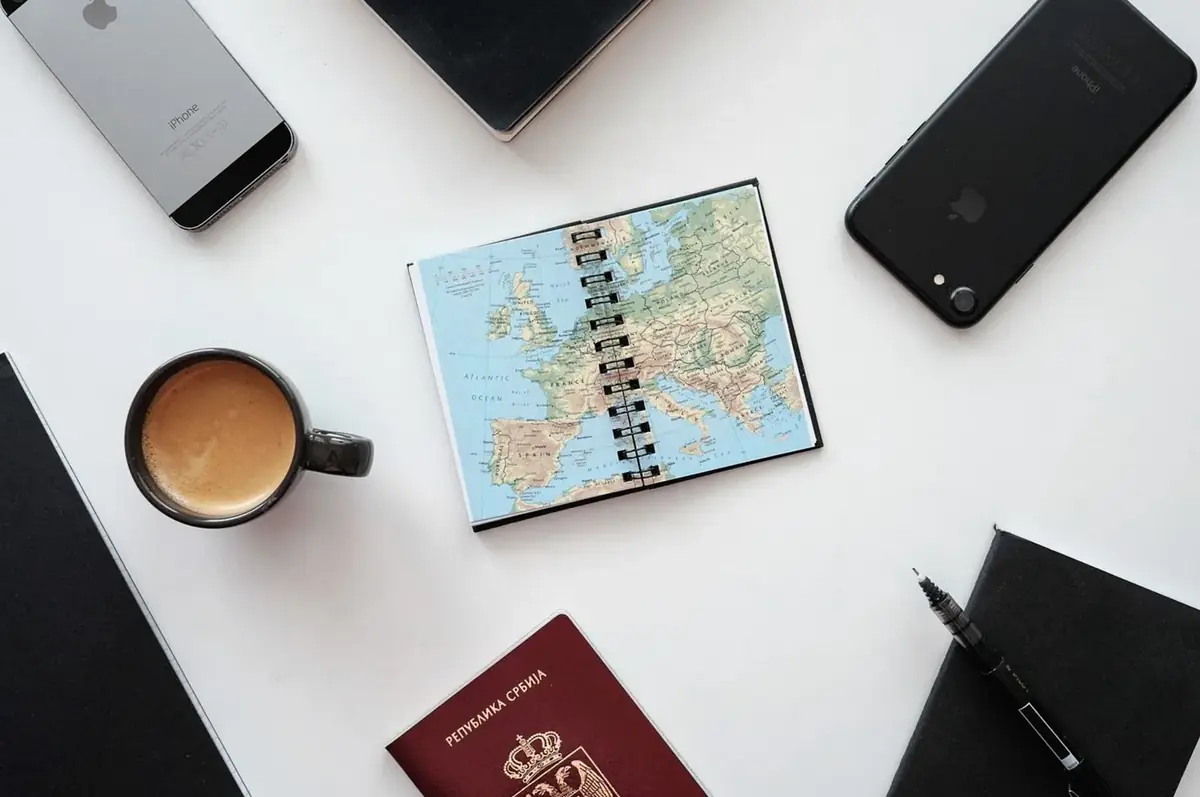 Notebook with a map, a coffee cup and phones on a white desk